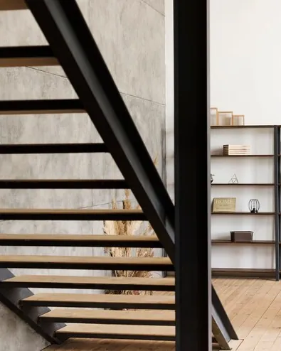 Scară minimalistă cu balustradă neagră lângă un raft deschis și pereți de beton aparent