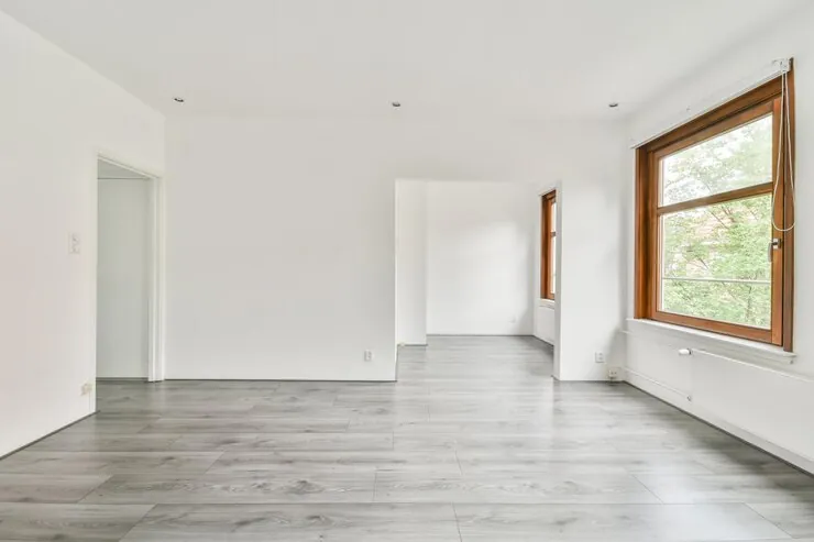 Apartament gol în variantă albă, cu pereți albi, parchet gri și o fereastră cu toc de lemn